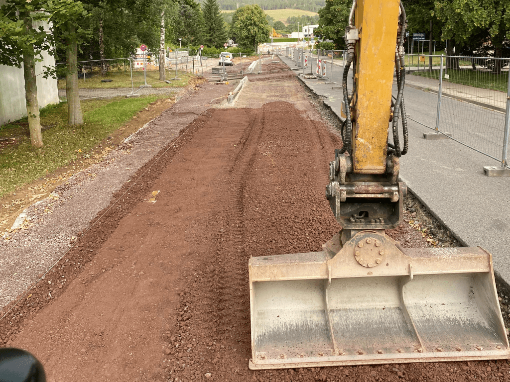 Baustelle für den Straßenbau mit einer Planierraupe, die auf einem vorbereiteten Untergrund aus rotem Schotter arbeitet.