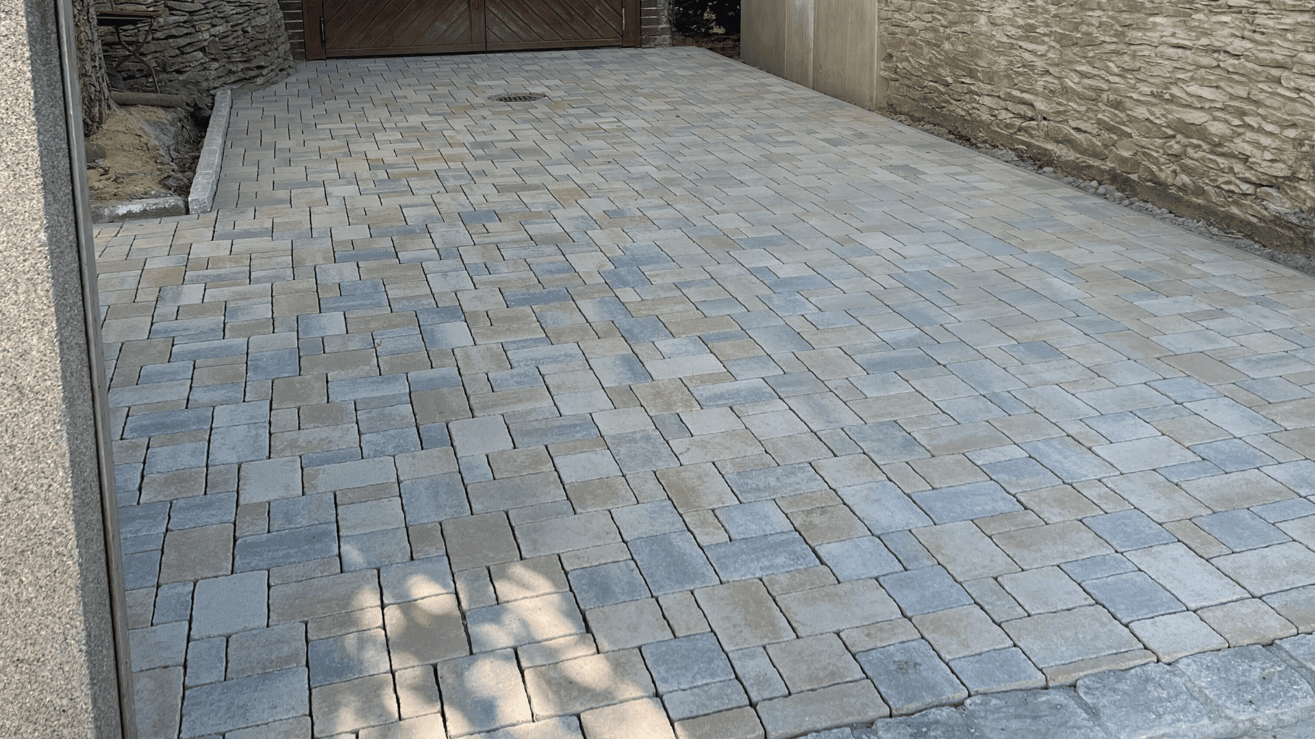 Neu gepflasterter Hofbereich mit grauen Steinen, angrenzend an ein gelbes Haus und eine vorbereitete Gartenfläche.