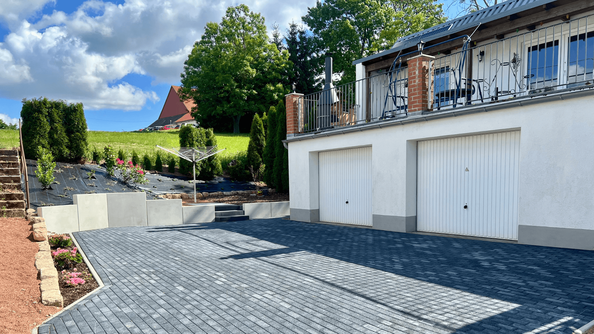 Neu gestaltete Außenanlage mit moderner Pflasterung, Hangbepflanzung und stilvoller Terrassengestaltung.