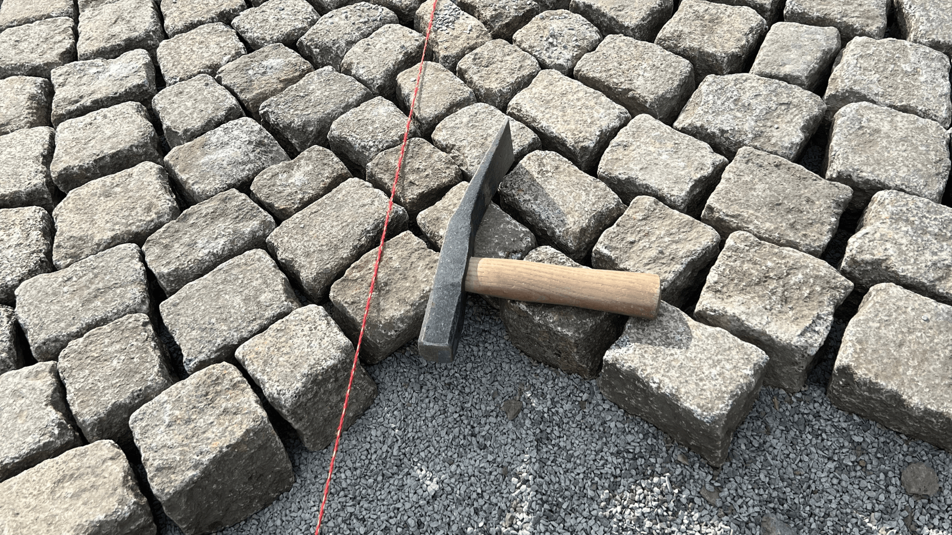 Natursteinpflaster in Handarbeit mit Hammer und Richtschnur beim Verlegen.