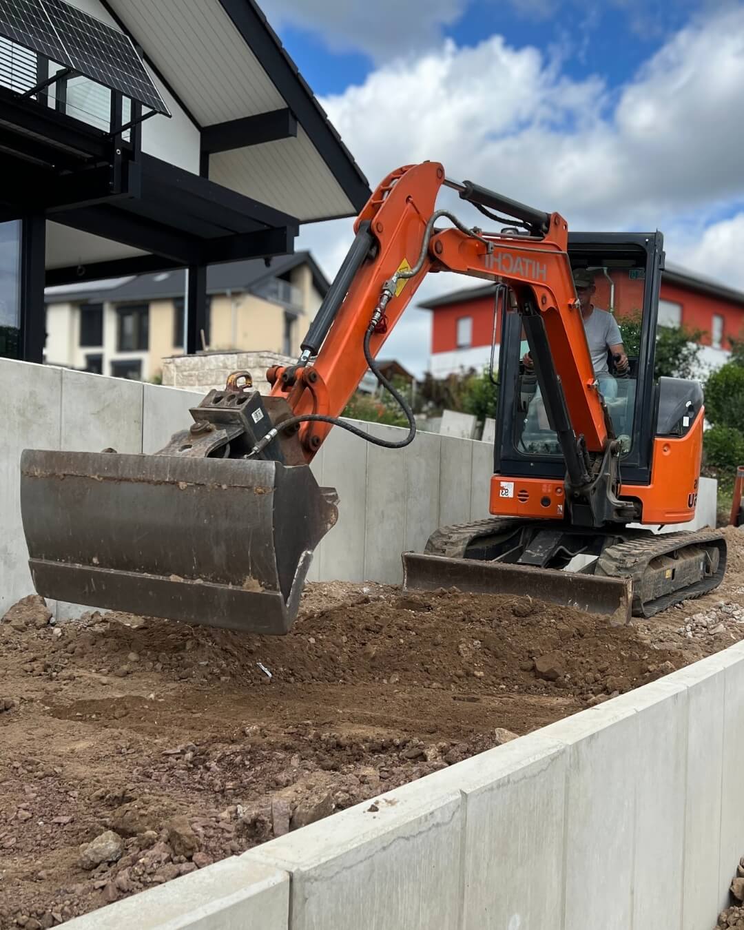 Baggerbild Frank Zwei Männer in Arbeitskleidung mit gelbem Bagger-Logo stehen vor einer Ziegelwand.